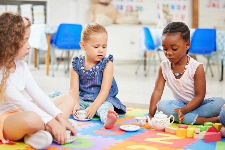 Group of diverse adorable little girls sitting cross legged on the floor in preschool and having a